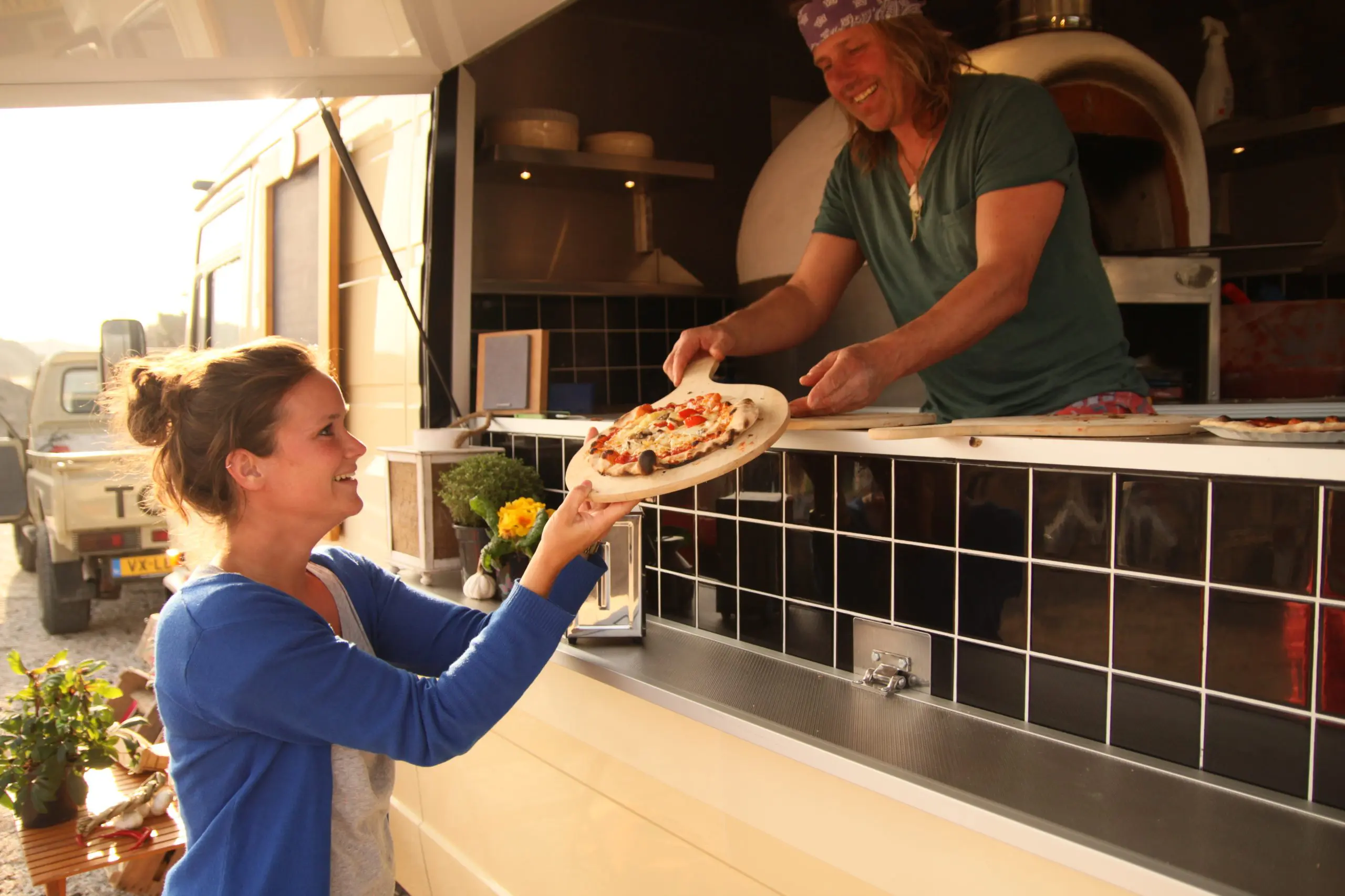 Pizza geserveerd door een pizza chef aan vrouw die blij kijkt.