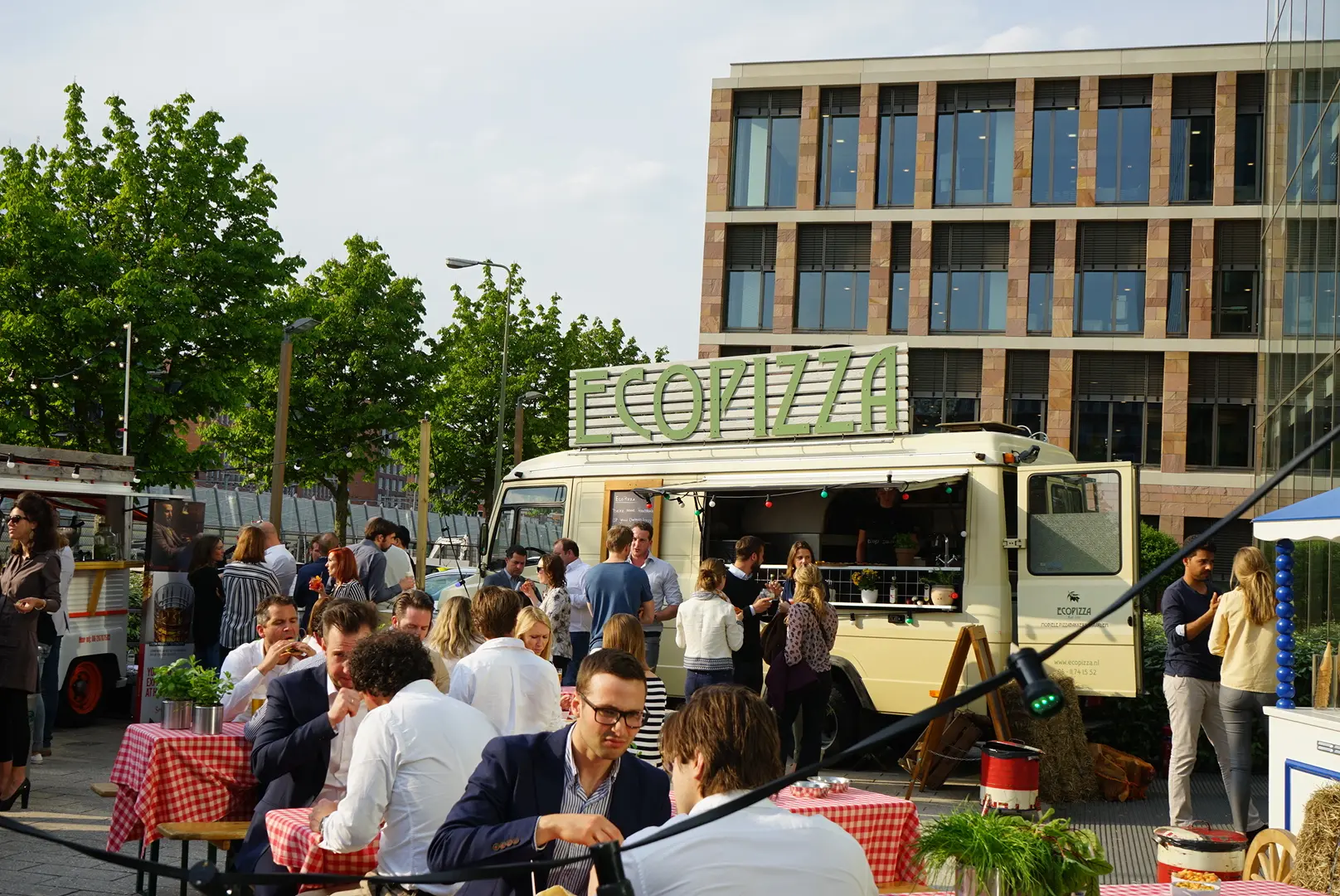Gasten aan tafels bij een lichte pizzatruck voor een modern kantoorgebouw