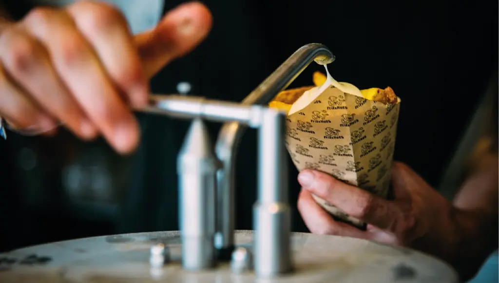 Saus wordt op een puntzak verse friet gepompt, een populair vrijmibo hapje