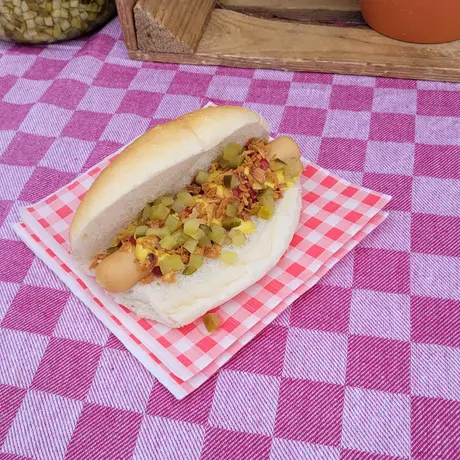 Broodje worst op een wit puntje met augurk, gefrituurde uitjes en saus