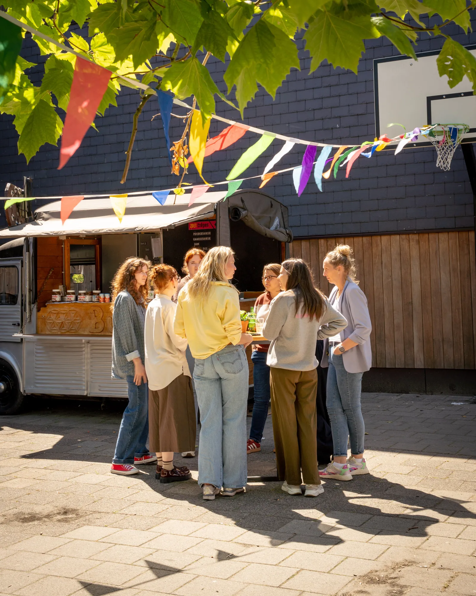 Groep collega's bestelt bij een witte vintage foodtruck op een schoolplein