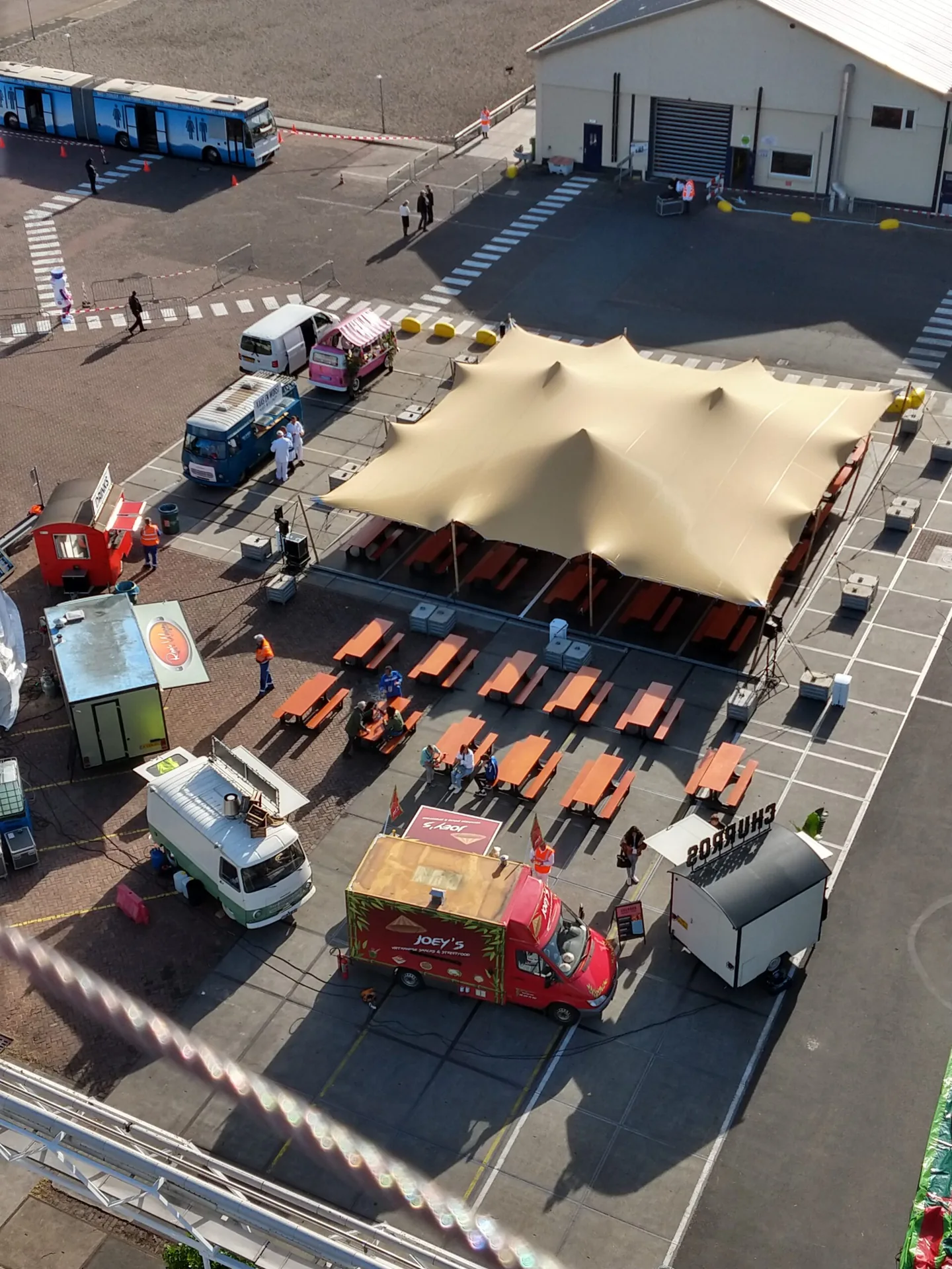 Foodtrucks en een stretchtent met picknicktafels op de parkeerplaats van een bedrijf tijdens een personeelsfeest