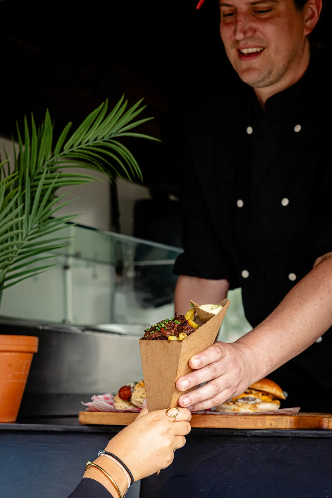 Kok overhandigt een puntzak met friet en stoofvlees vanuit de foodtruck