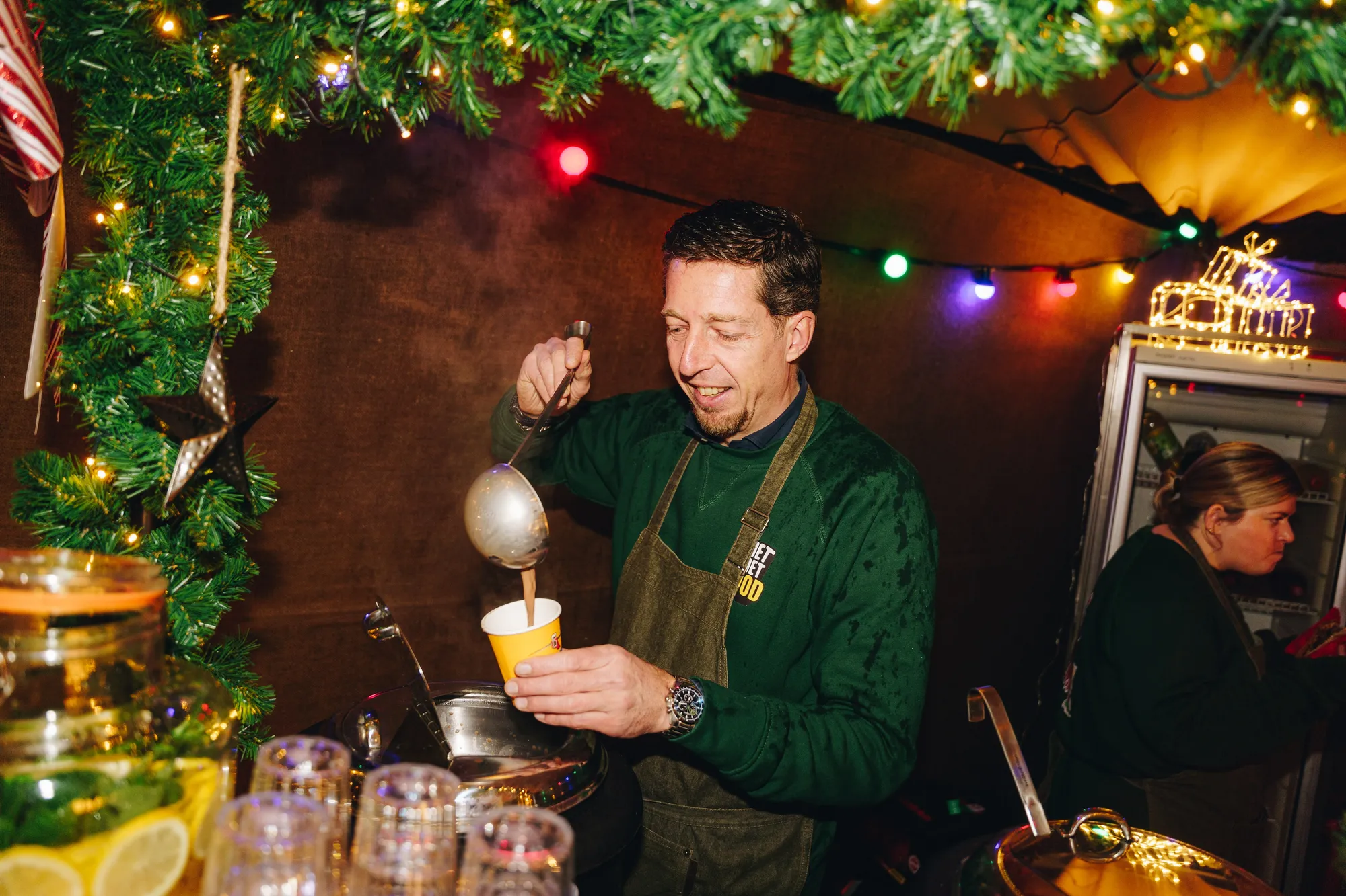 Medewerker schept een warme winterdrank in een beker bij een verlichte stand