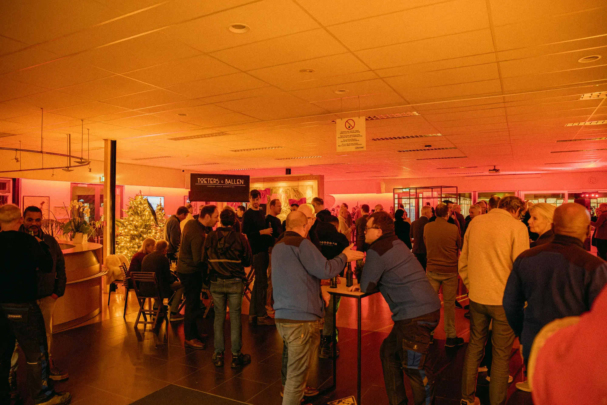 Gasten aan statafels tijdens een winterse vrijmibo binnen op kantoor met warm rood licht