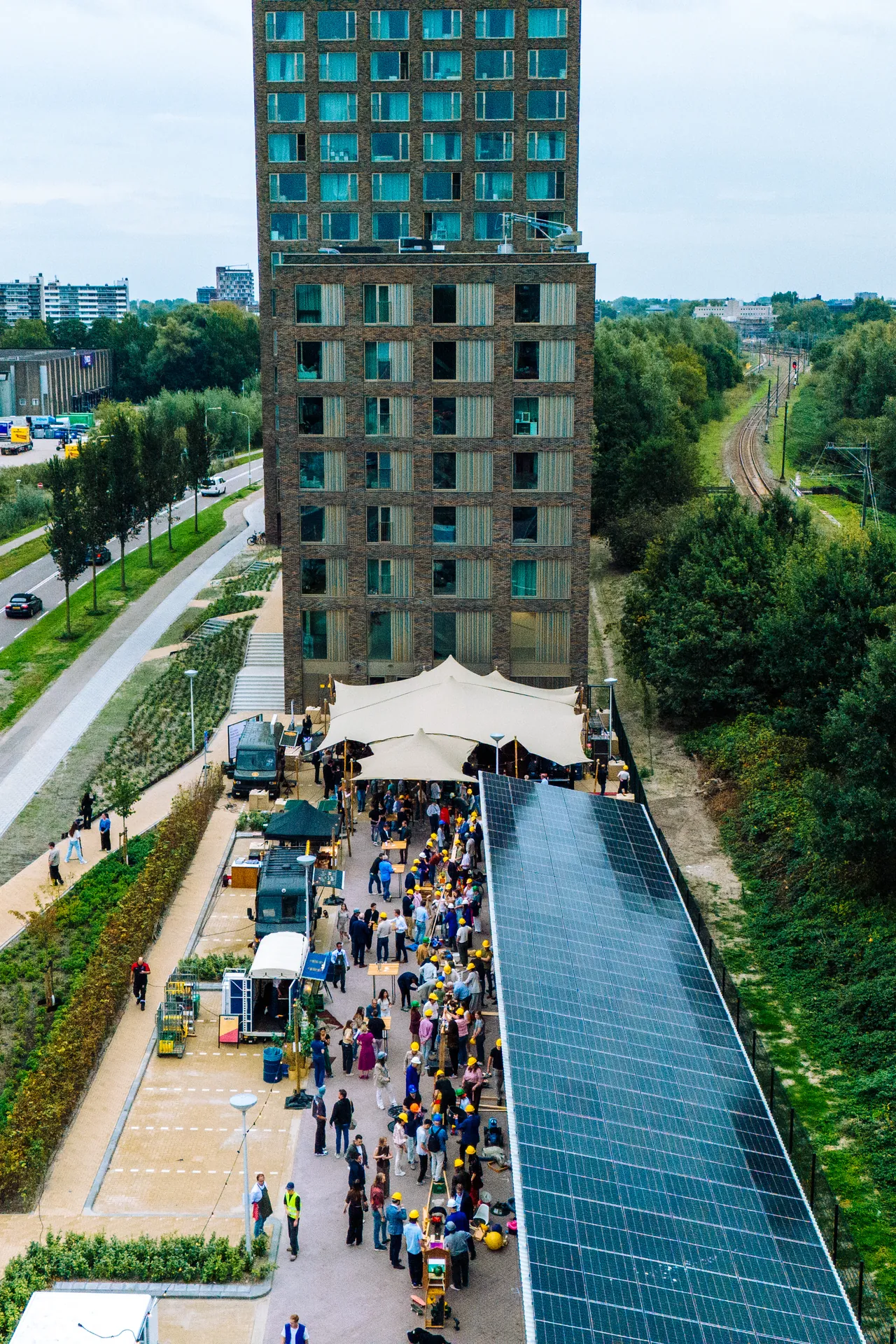 Dronefoto van een bouwevent met foodtrucks, tent en gasten naast een nieuwbouwtoren