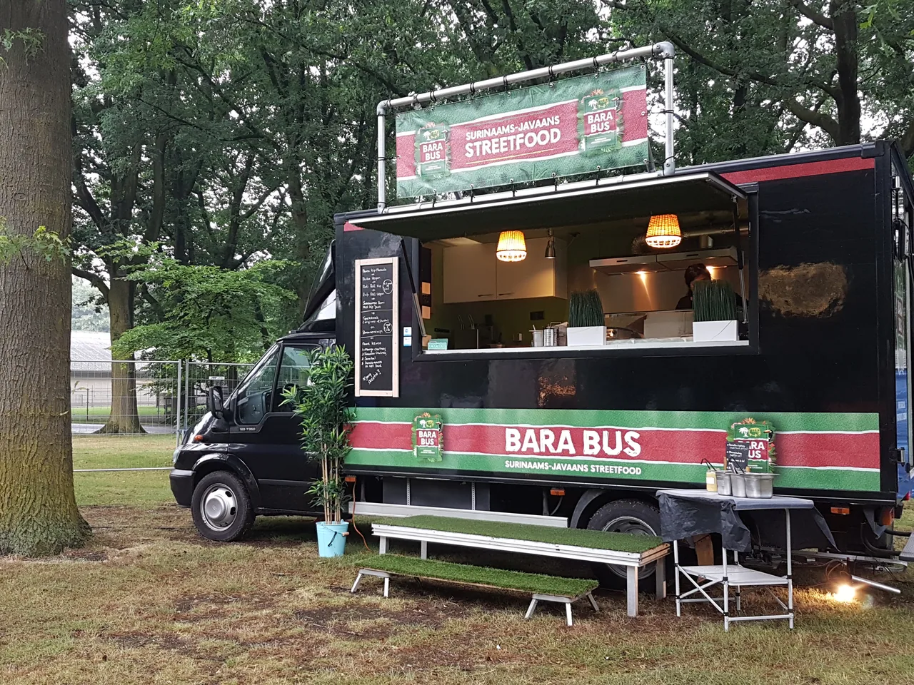 Zwarte Barabus foodtruck met verlichting en zitbanken op een evenemententerrein