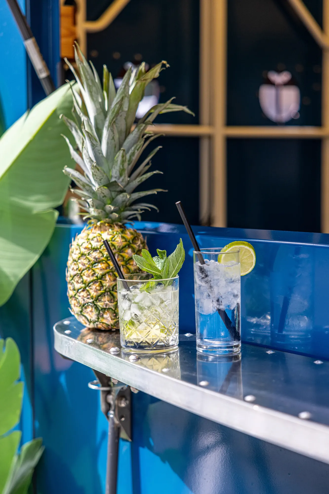 Twee verfrissende drankjes met munt en limoen naast een ananas op de bar van een blauwe dranktruck
