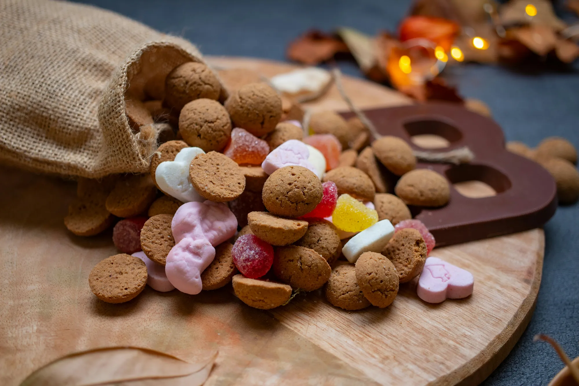Jute zak met pepernoten, schuimpjes en een chocoladeletter op een houten plank