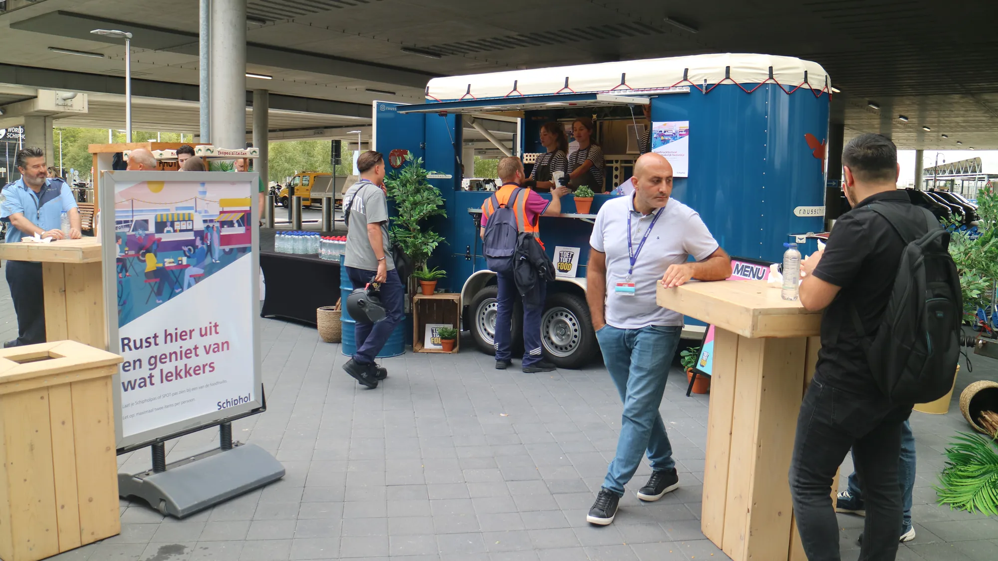 Schiphol-medewerkers halen iets lekkers bij een blauwe foodtruck tijdens een foodtruckfestival als bedankje
